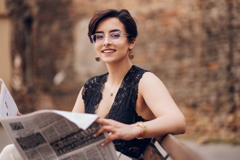 Portrait de mode en plein air d'une jeune femme élégante portant des vêtements à la mode tout en lisant le journal et assise sur un banc. 
