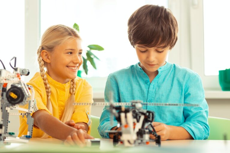 Une fille souriante donne des conseils à son camarade de classe sur la construction d'un ensemble de construction lors de leur cours de sciences