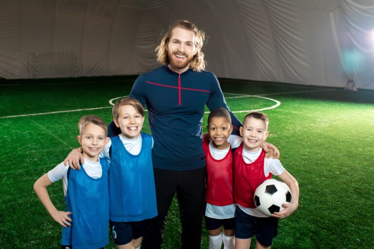 Entraîneur de football réussi et quatre garçons heureux en uniforme debout sur un terrain de football vert
