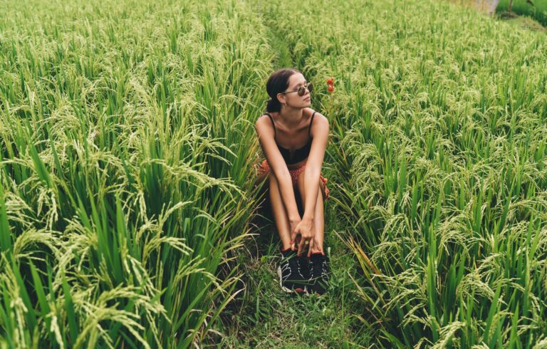 Corps complet d'une jeune voyageuse paisible portant des lunettes de soleil se relaxant dans une prairie rurale verdoyante pittoresque et profitant des vacances d'été à la campagne