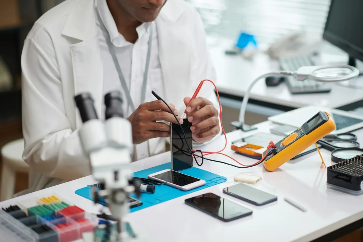 Image recadrée d'un réparateur vérifiant la batterie d'un smartphone à l'aide d'un multimètre